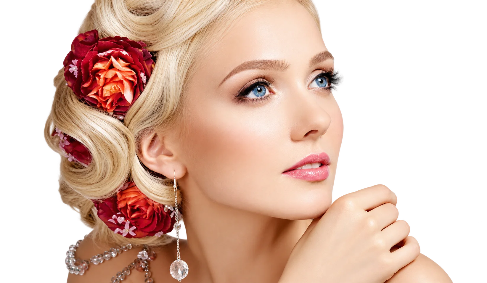 Portrait d'une jeune femme blonde aux yeux bleus, coiffée en boucles ondulées ornées de fleurs rouges, la main près du menton, sur fond blanc.